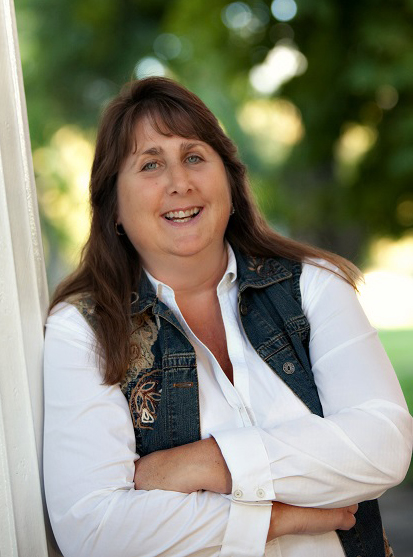 Image of Lindsay Andrus with arms folded, leaning against a doorframe with trees blurred in the background