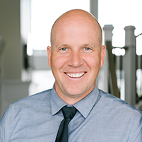 Image of Jason night in a blue shirt and tie leaning against a doorframe