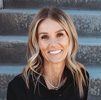 Image of Kim Harris smiling, sitting on stairs in black professional dress